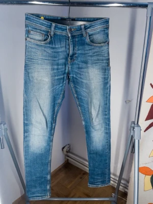 Ljusblå slim fit jeans 29/32 - Snygga ljusblå slim fit jeans i stretchigt material med klassisk femficksdesign och en trendig look. Jeansen har gylf med dragkedja och knapp, samt kontrastsömmar. Perfekta för en avslappnad och modern stil.
