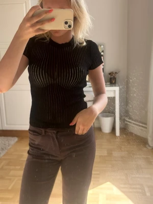 Svart ribbad topp med kort ärm💖💖 - Säljer en svart ribbad topp med korta ärmar och rund hals. Toppen har ett slim fit och vertikala ränder som ger en snygg struktur. Perfekt att matcha med jeans eller kjol för en cool look.