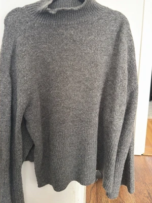Grå stickad polotröja med slits - Mysig grå stickad polotröja från Gina Tricot med ribbad hög krage och ribbade muddar. Tröjan har en avslappnad passform och är perfekt för kyliga dagar. Materialet känns mjukt och värmande, och färgen är lätt att matcha till olika outfits.