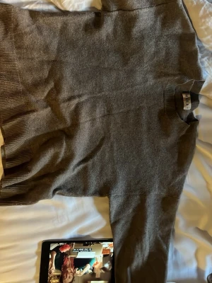 Beige/grå rundhalsad tröja från Wera - Mjuk och stilren grå tröja från Wera med rund halsringning och breda ribbade muddar vid ärmslut och nederkant. Perfekt för en clean och avslappnad look. Materialet ser ut att vara ull eller en ullmix.