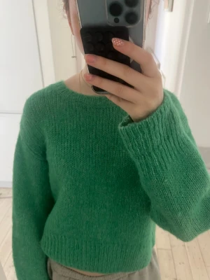 Grön stickad tröja med rund hals - Mjuk och fluffig grön stickad tröja med rund halsringning och långa ärmar. Tröjan har en enkel design utan mönster och är något kortare i modellen. Perfekt för dig som gillar en chill och cozy look.