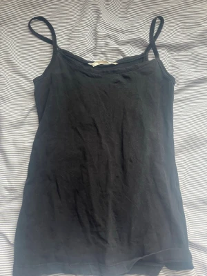 Svart linnetopp från H&M L.O.G.G. - En enkel svart linnetopp från H&M L.O.G.G. med smala axelband och rak passform. Tillverkad i mjuk bomull som känns skön mot huden. Perfekt att styla lager på lager eller bära som den är under varma dagar.