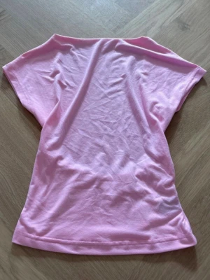 Ljusrosa topp med öppen rygg - Cool ljusrosa topp med öppen rygg och korta ärmar. Perfekt för dig som vill ha en enkel men ändå unik look. Materialet är mjukt och känns skönt mot huden, troligen bomull. Passformen är normal och toppen har en elastisk detalj bak.