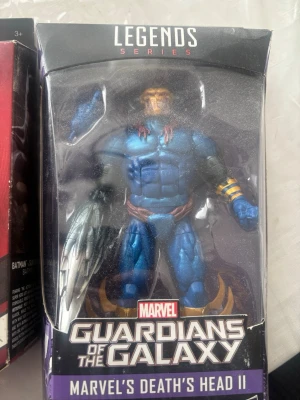 Guardians of the Galaxy Death's Head II - Säljer en actionfigur från Marvel Legends Series, Guardians of the Galaxy: Death's Head II. Figuren är blå med guld- och silverdetaljer, muskulös och har en futuristisk rustning. Perfekt för samlare eller fans av Marvel-universumet.