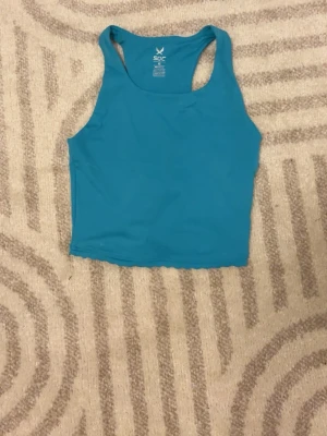 Turkos cropped tränings topp  från SOC - Cool turkos cropped tanktop från SOC med brottarrygg. Perfekt för att matcha med till träning. Materialet är mjukt och stretchigt, vilket gör den bekväm att bära hela dagen. Enkel design utan tryck eller mönster.