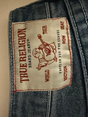 Blå jeans från True Religion - Säljer ett par klassiska blå jeans från True Religion med snygga kontrastsömmar. Jeansen har en design och är tillverkade i slitstarkt denim-material använd bara någon gång men tyckte längden var för lång och inte satt så bra i midjan. 