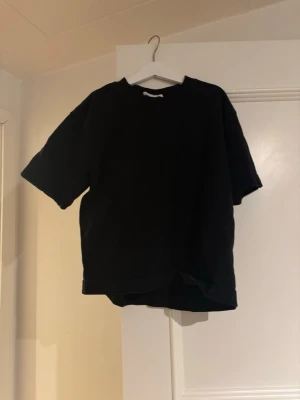 Svart basic t-shirt från Gina Tricot - En svart basic t-shirt från Gina Tricot, basically basics-kollektionen. T-shirten har en klassisk rund halsringning och korta ärmar. Perfekt till alla outfits och enkel att styla. Tillverkad i mjuk bomull för skön känsla.