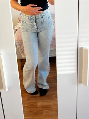 Ljusblå bootcut jeans med stora fickor - Säljer ett par ljusblå bootcut jeans med stora framfickor och hög midja. Jeansen har klassisk denimlook och är tillverkade i bomull. Perfekt för dig som gillar en avslappnad och trendig stil.