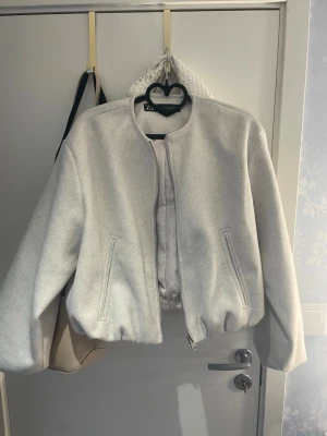 Den populära Zara bomberjacka!!🥰 - Endast använd en gång. Trendig beige bomberjacka från Zara med croppad passform och dragkedja framtill. Jackan har två snedställda fickor och elastisk midja för en snygg siluett. Perfekt för dig som vill ha en stilren och enkel look.
