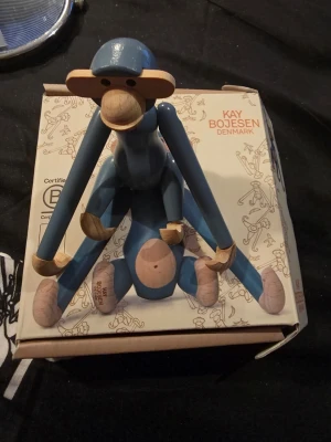 Blå trämjukisapa Kay Bojesen - Säljer en ikonisk blå apa i trä från Kay Bojesen Denmark. Apan har rörliga armar och ben, och är tillverkad i blåmålat och naturfärgat trä. Perfekt som inredningsdetalj eller samlarobjekt. Levereras i originalkartong.