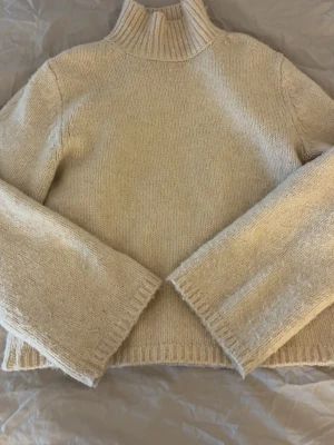 Beige stickad tröja från H&M - Säljer en beige stickad tröja från H&M med hög krage och långa ärmar. Tröjan har en enkel och stilren design med ribbstickade detaljer vid krage, ärmslut och nederkant. Perfekt för lager-på-lager och att hålla sig varm under kyliga dagar. Sitter som en s💓