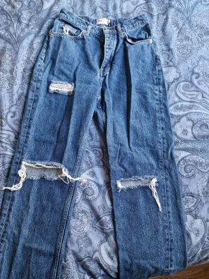 Blåa ripped jeans från NA-KD - Ett par blåa jeans från NA-KD Reborn med slitna detaljer och raka ben. Passar bra för en avslappnad stil.