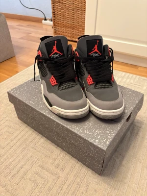 Air Jordan 4 Retro Infrared  - Snygga Air Jordan 4 Retro sneakers i färgerna mörkgrå, svart och Infrared 23. Skorna har klassisk mesh och läderdetaljer, samt den ikoniska Jumpman-loggan på plösen. Perfekta för dig som gillar streetwear och vill sticka ut med en tidlös modell. Storlek 43. Knappt använda 