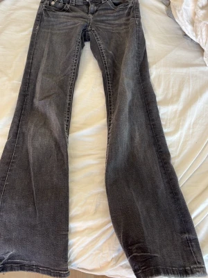 Bootcut jeans i mörkgrå denim - Bootcut jeans i mörkgrå tvättad denim med klassiska fem fickor och kontrastsömmar. Jeansen har en låg midja och utsvängda ben, perfekt för en avslappnad och trendig look. Materialet är bomullsdenim och passformen är bekväm.