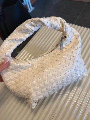Vit flätad handväska Ginatricot  - Säljer en snygg vit handväska från Pieces i flätad design. Väskan har ett kort handtag och dragkedja upptill. Tillverkad i konstläder som ger en trendig look. Perfekt accessoar för att lyfta din outfit.