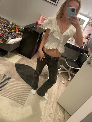 Vit volangblus med v-ringning - Söt vit topp med djup v-ringning och volangdetaljer. Kort modell med puffiga ärmar och resår i midjan för en feminin siluett. Perfekt till jeans eller kjol. Materialet ser ut att vara bomull eller bomullsblandning. (Ej struken på bilden)