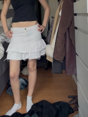 Vit volangkjol🤍 - Säljer en vit jeanskjol kortkjol med volanger. Kjolen har knappar och fransig nederkant som ger en cool och trendig look. Perfekt för dig som gillar att sticka ut och vill ha något unikt i garderoben!