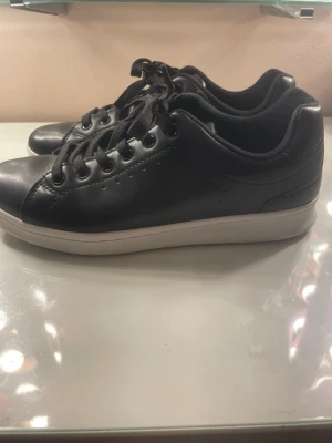 Svarta sneakers med vit sula - Stilrena svarta sneakers med vit sula och svarta skosnören. Skorna har en klassisk låg profil och är tillverkade i slätt syntetläder. Perfekta för dig som gillar en clean och enkel look till vardagsoutfiten.