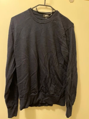 Svart tröja från Uniqlo - En enkel mörkblå tröja från Uniqlo med rund halsringning och långa ärmar. Tröjan har en klassisk passform och ribbade muddar vid ärmslut och nederkant. Perfekt att matcha med jeans eller kjol för en clean look.