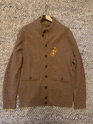  Stenströms cardigan - Mysig brun kofta från stenströms i mjuk merinoull. Koftan har ribbad krage, knäppning framtill med svarta knappar och två fickor med lock och knapp. Perfekt för lager på lager och en stilren look. Storlek xl men passar som L