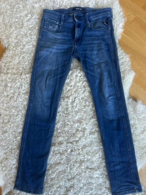 Blå skinny jeans från Replay - Säljer ett par blå skinny jeans från Replay med klassisk femficksdesign och dragkedjedetalj vid fickan. Jeansen har en snygg tvätt med slitningar och smal passform som sitter tajt längs benen. Perfekta för en trendig och avslappnad stil. Stl 28/32