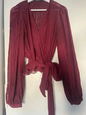 Vinröd omlottblus från Gina tricot - Vinröd omlottblus från Gina Tricot med långärmade, plisserade ärmar och v-ringning. Strl S. I mycket gott skick.
