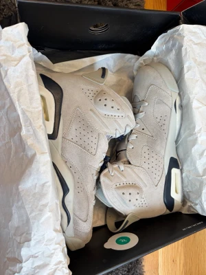 Air Jordan 6 Retro Beige Suede - Snygga Air Jordan 6 Retro sneakers i beige mocka med mörkblå detaljer och perforeringar på sidorna. Klassisk hög siluett med Jumpman-logo på hälen och robust sula. Perfekta för dig som vill sticka ut med stilrena och ikoniska sneakers.