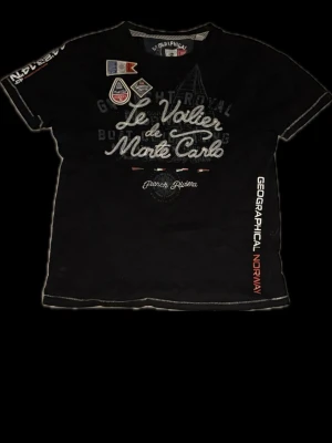 Geographical Norway t-shirt - Cool svart t-shirt från Geographical Norway med tryck och broderade detaljer framtill. Texten 'Le Voilier de Monte Carlo' och flera patchar ger en sportig vibe. Kortärmad modell med kontrastsömmar och tryck på ärm och sida.