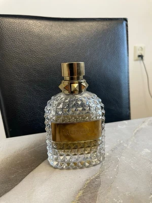 Valentino parfymflaska med guld - Elegant parfymflaska från Valentino med kristallmönstrad transparent glasdesign och detaljer i guld, inklusive en guldig platta med logotyp och en lyxig guldfärgad kork med nitar. Perfekt som statement på sminkbordet.