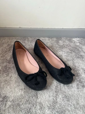 Svarta glittriga ballerinaskor med rosett - Svarta ballerinaskor med lite glitter. Köpta på vinted men skulle säga att de är i gott skick. 