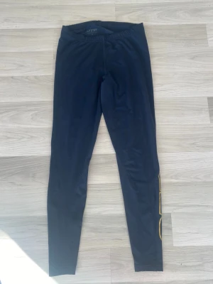 Träningsbyxor från OTP - Säljer ett par mörkblåa/svart träningsbyxor från OTP med guldiga detaljer. Byxorna har en sköna passform med raka ben. I storlek M