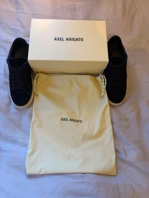 Svarta sneakers från Axel Arigato - Stilrena svarta sneakers från Axel Arigato med vit sula och klassisk snörning. Skorna har mocka vilket kan ge en lyxig känsla. Perfekta för dig som gillar en clean och modern look. Det som ingår är skorna, påse och skolåda. Storlek 41, väll omhändertagna. Skriv gärna vid intresse!