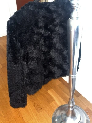 Svart fuskpälsjacka från Vero Moda - Säljer en svart fuskpälsjacka från Vero Moda. Jackan har rund halsringning, lång ärm och en mjuk, fluffig struktur. Perfekt för att hålla värmen under kalla dagar och ger en trendig look till din outfit. Ett l hål men inget som syns om man kan sy så är det lätt att fixa