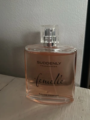 Suddenly Femelle Eau de Parfum - En elegant parfym från Suddenly med namnet Femelle. Flaskan är rektangulär med rundade kanter och har en transparent plastkork. Innehållet är ljusrosa och flaskan är gjord av glas. Perfekt för dig som gillar fräscha och feminina dofter.
