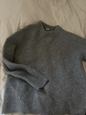 Grå stickad tröja i ullmix - Mysig grå stickad tröja med rund hals och ribbade muddar vid ärmslut och nederkant. Tröjan har en enkel och stilren design, perfekt för lager på lager. Tillverkad i mjuk ullmix som håller dig varm under kyliga dagar.