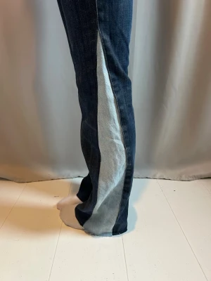 Mörkblå lågmidjade jeans med kontrastpanel - 🩵20% REA🩵Unika mörkblå jeans med ljusblå kontrastpanel längs utsidan av benen. Modellen har utsvängda ben och klassisk femficksdesign. Jeansen är tillverkade i denim och har en snygg knappgylf. Perfekta för dig som vill sticka ut med en cool detalj.🩵 innerbenslängden är 74cm och midjemåttet är 38cm rakt över🩵