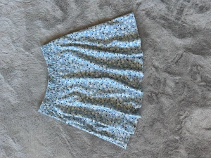 Blå blommig kjol med resårmidja - Söt ljusblå kjol med små vita och mörkblå blommor. Kjolen har en bekväm resår i midjan och är lätt utställd för en avslappnad look. Tillverkad i ett mjukt och stretchigt tyg som känns skönt mot huden. Funkar för både xs och s