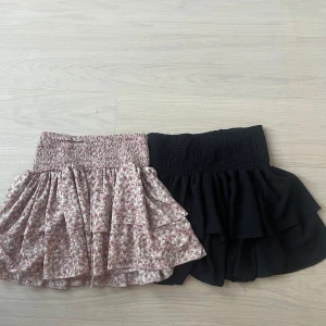Två volangkjolar  - Säljer två gulliga korta kjolar. Ena kjolen är svart och den andra är ljusrosa med små blommor i vitt. Båda är i storlek S. 150kr för båda 75kr för en. 