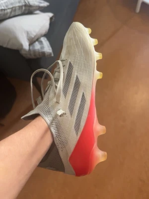 Adidas X Speedflow grå/röd fotbollssko. Gamla og skor som man inte hitta ofta just nu. - Snygg fotbollssko från Adidas X Speedflow-serien i grått med röda och svarta detaljer. Skon har låg vikt, snörning och en ovandel i syntetmaterial för bra bollkontroll. Sulan är gul-transparent och designad för maximalt grepp på planen. Perfekt för dig som vill ha speed och stil.