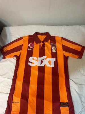 Galatasaray matchtröja Nike röd/gul - Galatasaray matchtröja från Nike med klassiska röda och gula vertikala ränder, klubbmärke och Nike-logga på bröstet samt sponsortryck. På ryggen står det 'ICARDI' och nummer 9. Tillverkad i lätt och ventilerande material, perfekt för fotbollsträning eller match.