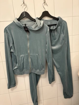 Blått velourset med hoodie och byxor - Mysigt loungewear-set i ljusblå velour från Bubbleroom. Setet består av en hoodie med dragkedja, fickor och resår i midjan samt matchande byxor med resår i midja och benslut. Perfekt för chill dagar hemma. Turkos