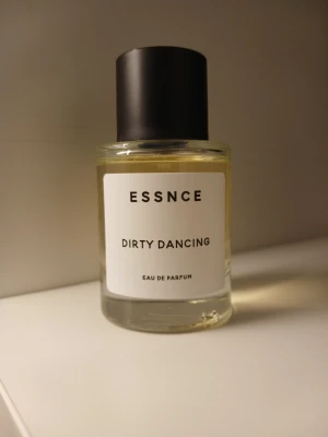 ESSNCE Dirty Dancing parfym💕 - ESSNCE Dirty Dancing Eau de Parfum i en stilren, rund glasflaska med svart lock. Parfymen har en minimalistisk vit etikett med svart text och innehållet är ljust gult. Perfekt för dig som gillar moderna och enkla designer.