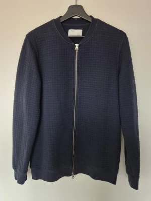 Samsøe Samsøe Mörkblå zip hoodie med struktur - Mörkblå hoodie med hel dragkedja framtill och diskret rutmönstrad struktur i tyget. Rund halsringning och ribbade muddar vid ärmslut och nederkant. Perfekt för en clean och stilren look.