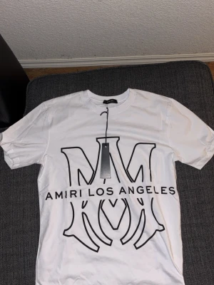 Vit Amiri t-shirt med stor logga - Säljer en vit t-shirt från Amiri med stor svart loga. Mycket fin och stilig passar bra med jeans. Aldrig använd köpte den i fel storlek. 
