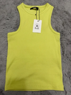 Ljusgul ribbad linnetopp BikBok - Snygg ljusgul ribbad linnetopp från BikBok. Toppen är ärmlös med rund halsringning och har en tight passform. Perfekt att styla med jeans eller kjol för en fräsch look.