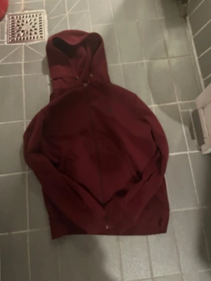 Vinröd hoodie med dragkedja - Snygg vinröd hoodie med dragkedja och huva. Klassisk modell med fickor framtill och justerbara snören i huvan. Perfekt för en avslappnad stil och enkel att matcha med jeans eller joggers.