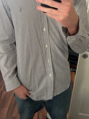 Randig skjorta ralph lauren - Snygg skjorta med smala vertikala ränder i vitt och mörkgrått. Klassisk krage och knäppning framtill. Långärmad modell som passar perfekt till jeans eller chinos. Tillverkad i mjukt bomullstyg för en bekväm känsla. Storlek S men kan passa M också! Tveka inte på frågor om pris👍