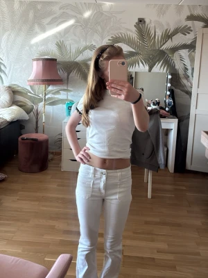 Vita utsvängda jeans med mid midja - Säljer ett par vita jeans från American Eagle. Jeansen har mid midja och  klassiska fickor fram och bak. Jeansen är köpta för 700kr nya i butik. Storleken står inte riktigt, men det passar mig som vanligtvis bär 32/34 (Jag  är 164cm).