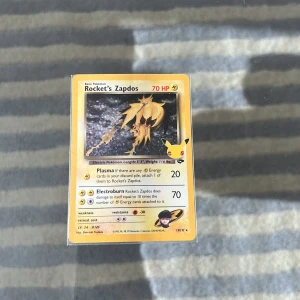 Rocket's Zapdos Pokémonkort - Säljer ett Rocket's Zapdos samlarkort från Pokémon TCG. Kortet har gul ram, svart text och en bild på Zapdos i mitten. Det är tryckt på klassiskt glansigt papp och har 70 HP. Kortet har detaljer på engelska och är från Team Rocket-serien.