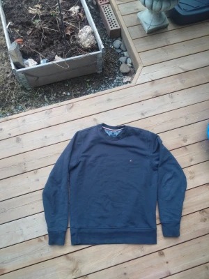 Mörkblå sweatshirt från Tommy Hilfiger - Mörkblå sweatshirt från Tommy Hilfiger med klassisk rund halsringning och diskret logga broderad på bröstet. Tröjan har långa ärmar och är tillverkad i mjuk bomull för en skön och avslappnad stil.